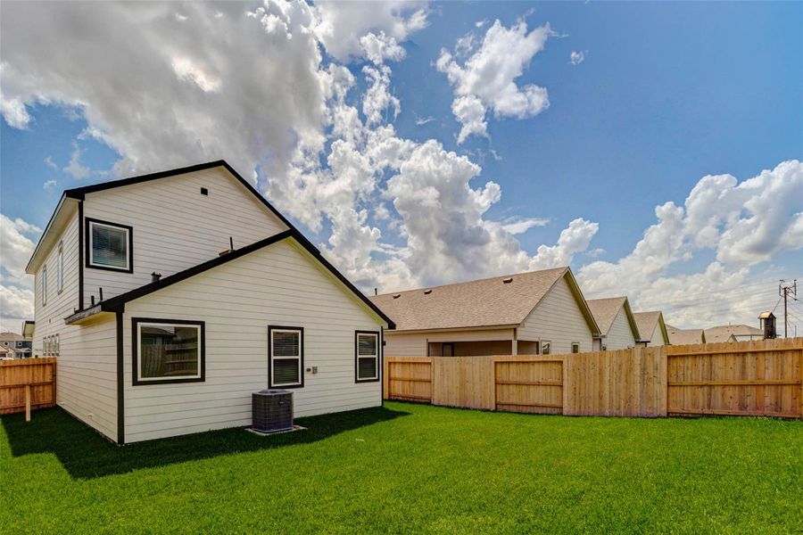 Angled backyard view featuring a wide green lawn, full wood privacy fencing, rear home elevation, and open sky above. The outdoor area offers room for recreation, pets, gardening, or a future seating area, creating a practical extension of the home’s living space.
