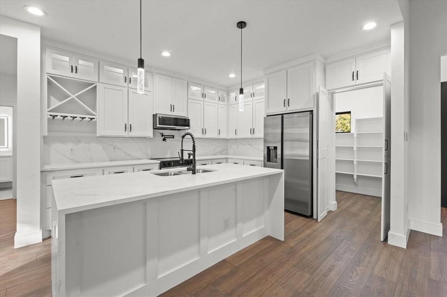 Kitchen with appliances with stainless steel finishes, backsplash, dark wood-type flooring, white cabinetry, and an island with sink