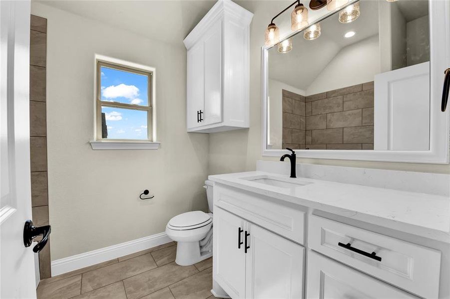 Bathroom featuring vanity, toilet, lofted ceiling, and tile patterned flooring