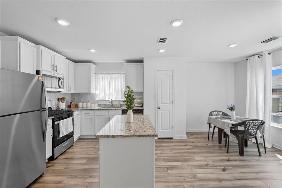 Kitchen with stainless steel appliances, a center island, light stone counters, white cabinets, and light wood-style flooring