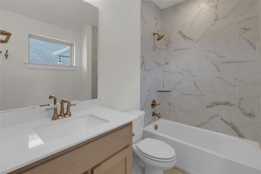 Bathroom featuring a light wood-finish vanity with a white countertop and undermount sink, brass-finish fixtures, and a white tile surround bathtub with a built-in shelf