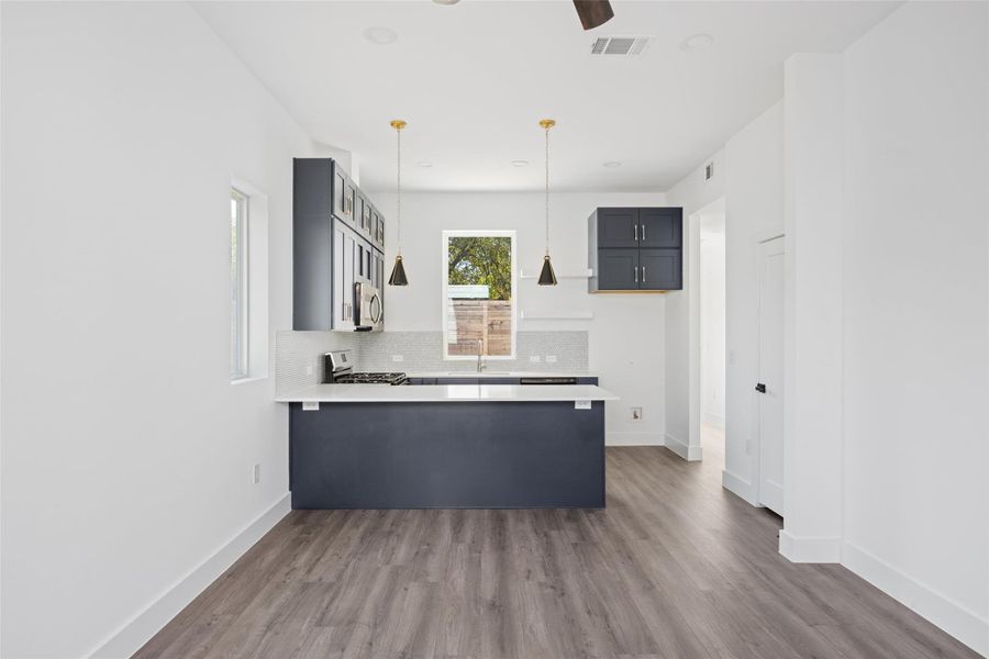 Kitchen featuring a peninsula, dark wood-type flooring, backsplash, and pendant lighting Kitchen featuring a peninsula, dark wood-type flooring, backsplash, and pendant lighting