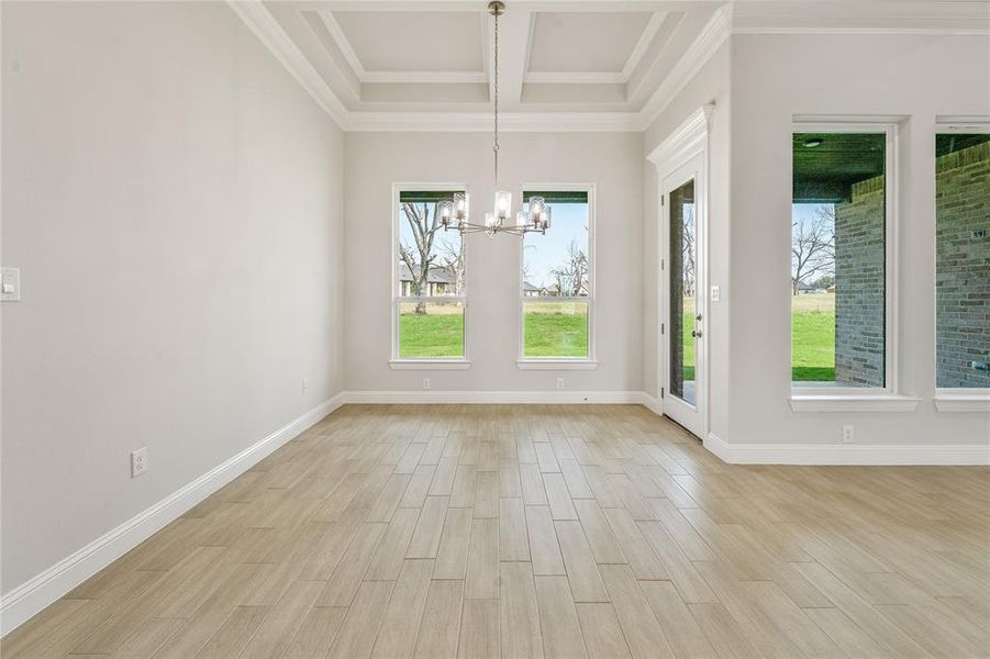 Unfurnished dining area with wood finish floors, a chandelier, beamed ceiling, coffered ceiling, and crown molding
