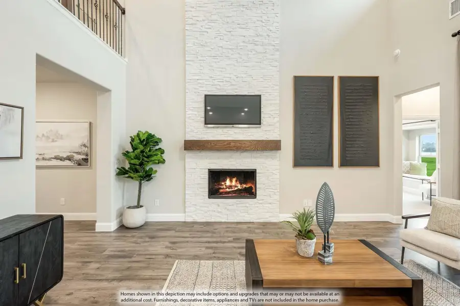 Living room with two-story white stone fireplace, wood mantel, wall-mounted TV, and hardwood floors