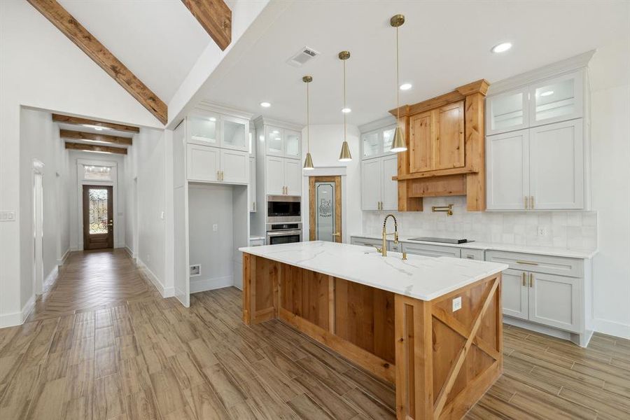 Kitchen featuring decorative backsplash, an island with sink, light stone countertops, white cabinetry, and appliances with stainless steel finishes