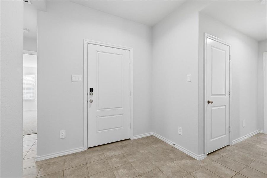 Foyer entrance featuring baseboards and light tile patterned flooring, garage door to the right and front bedroom to the left Foyer entrance featuring baseboards and light tile patterned flooring, garage door to the right and front bedroom to the left