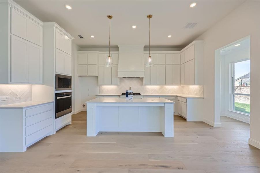 Kitchen with light wood-type flooring, white cabinetry, appliances with stainless steel finishes, and tasteful backsplash