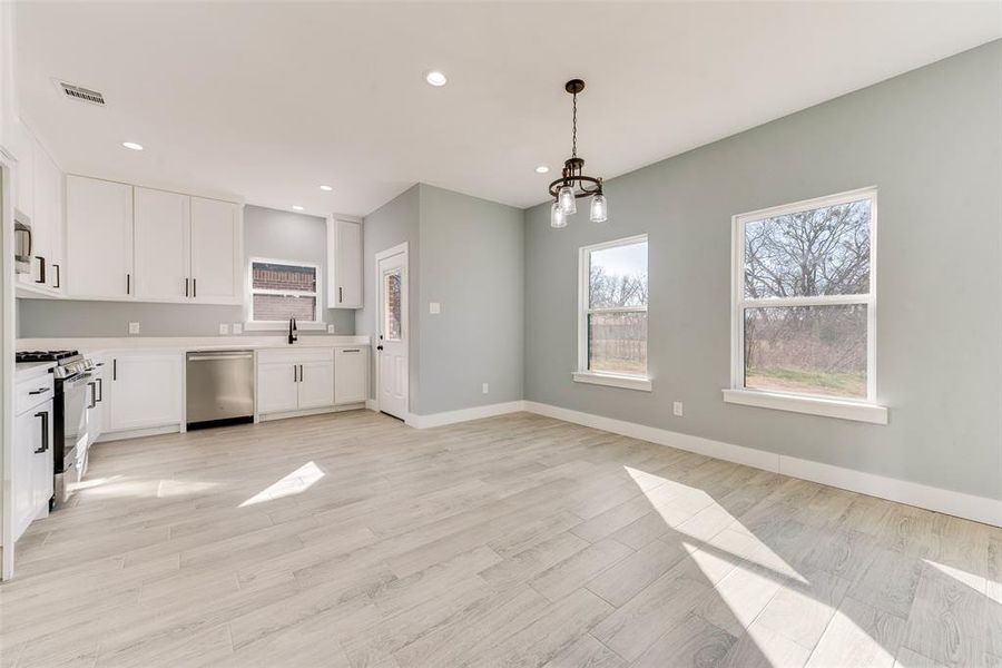 Kitchen with pendant lighting, sink, appliances with stainless steel finishes, an inviting chandelier, and white cabinets