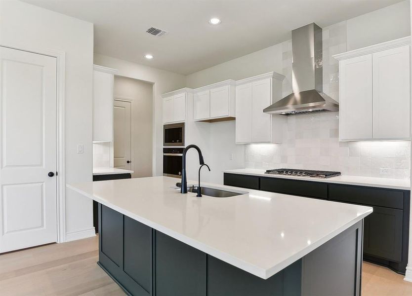 Modern kitchen featuring a large island with a sink and dark cabinetry, white upper cabinets, stainless steel appliances, and light-colored flooring