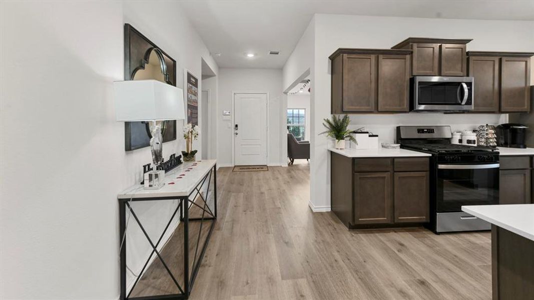 Open-concept kitchen and entryway featuring wood-finish flooring, dark wood cabinetry, stainless steel appliances, and light countertops Open-concept kitchen and entryway featuring wood-finish flooring, dark wood cabinetry, stainless steel appliances, and light countertops
