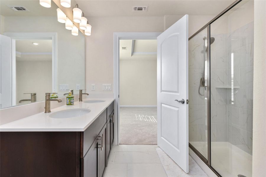 Bathroom featuring double vanity, a marble finish shower, light marble finish flooring, and light colored carpet