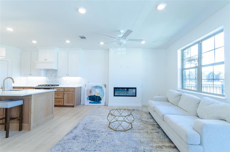 Living room with light wood-style floors, recessed lighting, a ceiling fan, and a glass covered fireplace