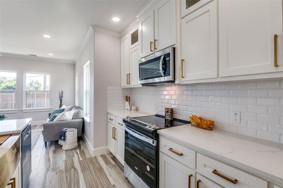 Kitchen with ornamental molding, light stone countertops, tasteful backsplash, stainless steel appliances, and white cabinets