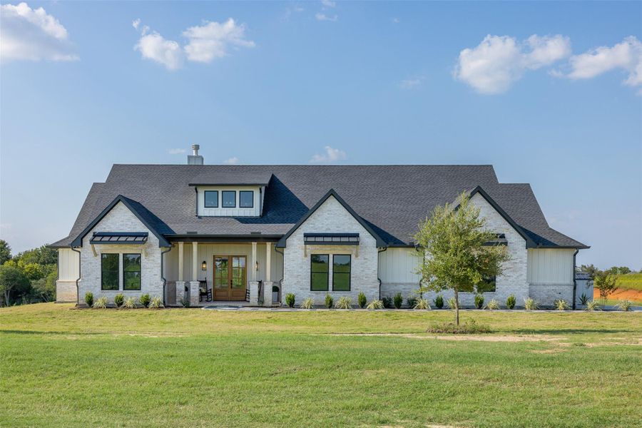 Modern farmhouse with a porch, board and batten siding, a front yard, a chimney, and roof with shingles