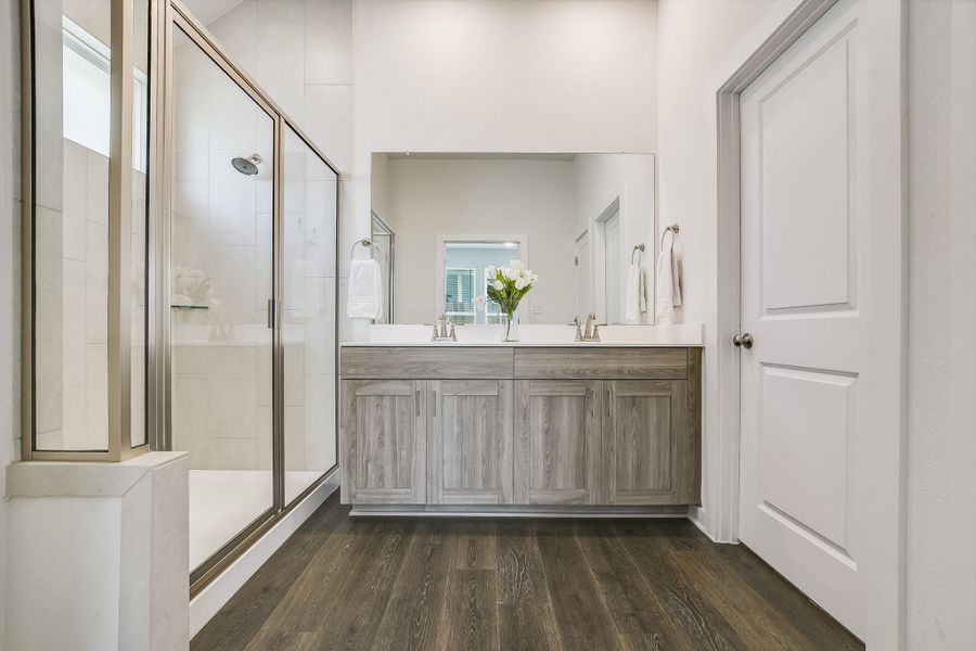 Spacious bathroom featuring a dual vanity with a light wood-finish cabinet, a large frameless mirror, and a glass-enclosed shower with a high window