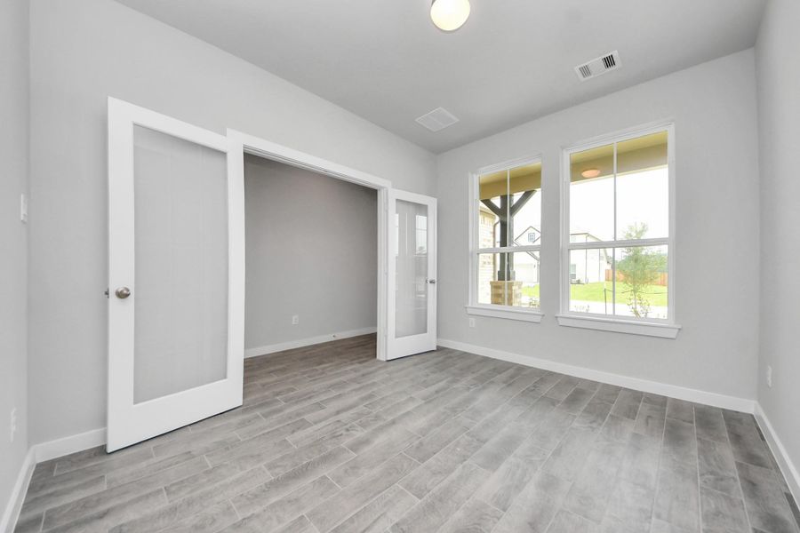 Perfect blend of sophistication and warmth in this home office, boasting elegant wood-look tile flooring and flooded with natural light from expansive windows and French doors. Sample photo of completed home with similar floor plan. Actual colors and selections may vary.