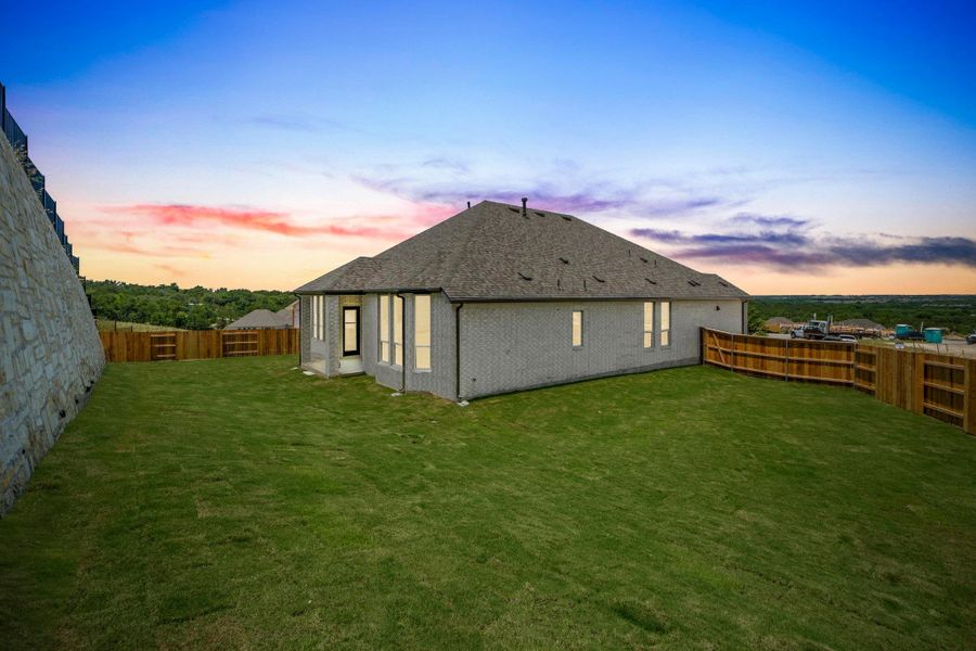 Back of house at dusk featuring brick siding, a fenced backyard, and a shingled roof