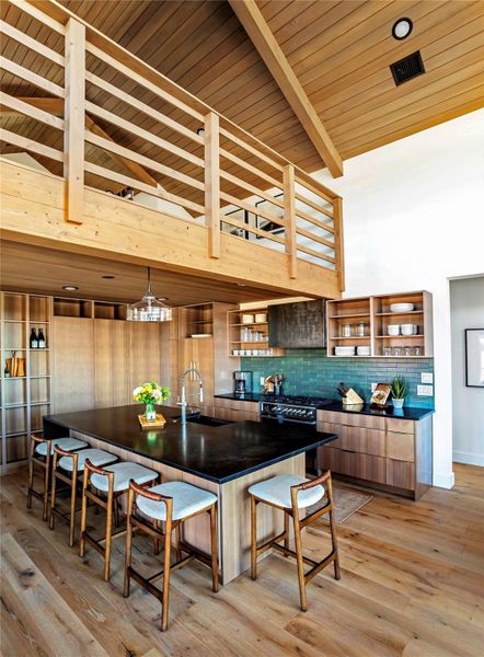Spacious chef’s kitchen with oversized island, custom cabinetry, open shelving, and loft overlook above the main living space.
