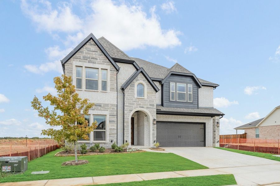 Two-story home with light stone exterior, dark trim, two-car garage, and manicured front lawn