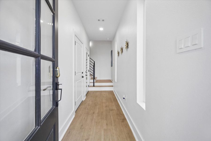 Glass and black steel front door sets the tone at the entry. Wood look plank floors run the length of the hall toward the stairs, lit by recessed cans. Glass and black steel front door sets the tone at the entry. Wood look plank floors run the length of the hall toward the stairs, lit by recessed cans.