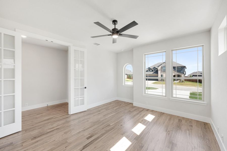Empty bedroom with hardwood floors, ceiling fan, large windows, and French doors leading to a closet