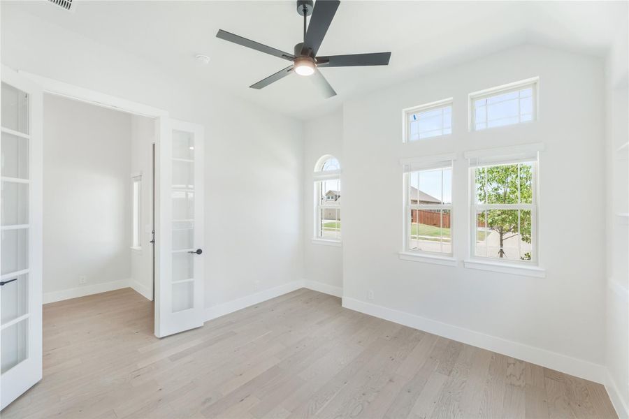 Empty room with light hardwood floors, ceiling fan, white walls, and multiple windows with natural light. Empty room with light hardwood floors, ceiling fan, white walls, and multiple windows with natural light.