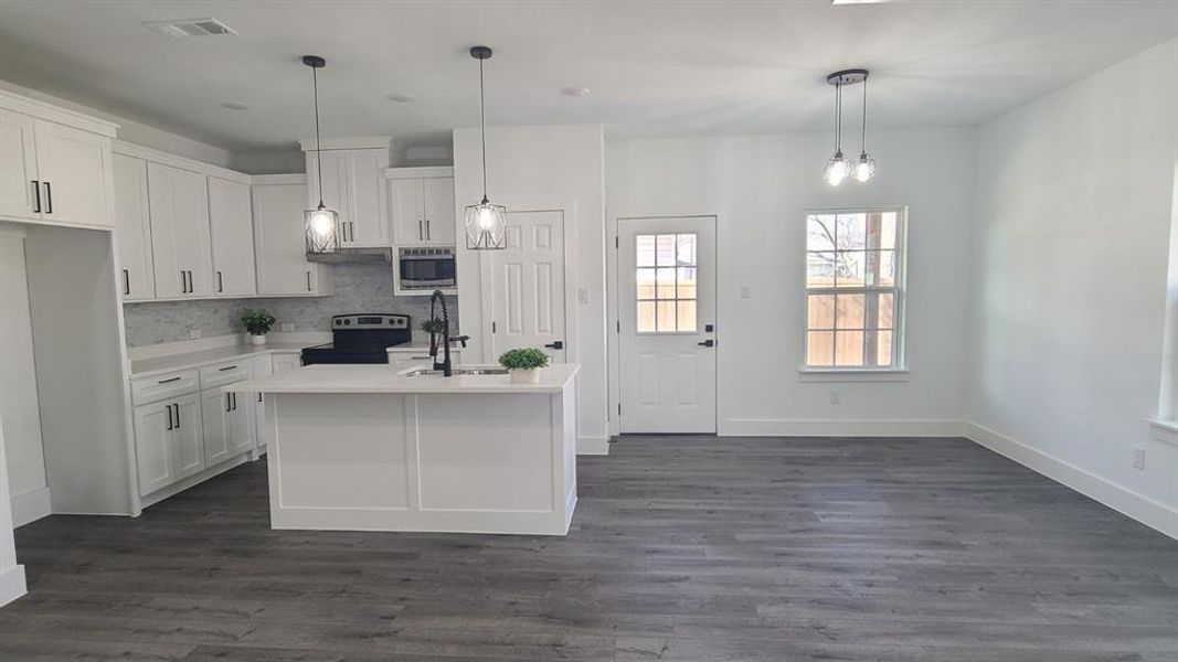 Open-concept living space featuring a modern kitchen with white cabinetry, a center island with sink, stainless steel appliances, and a tile backsplash Open-concept living space featuring a modern kitchen with white cabinetry, a center island with sink, stainless steel appliances, and a tile backsplash