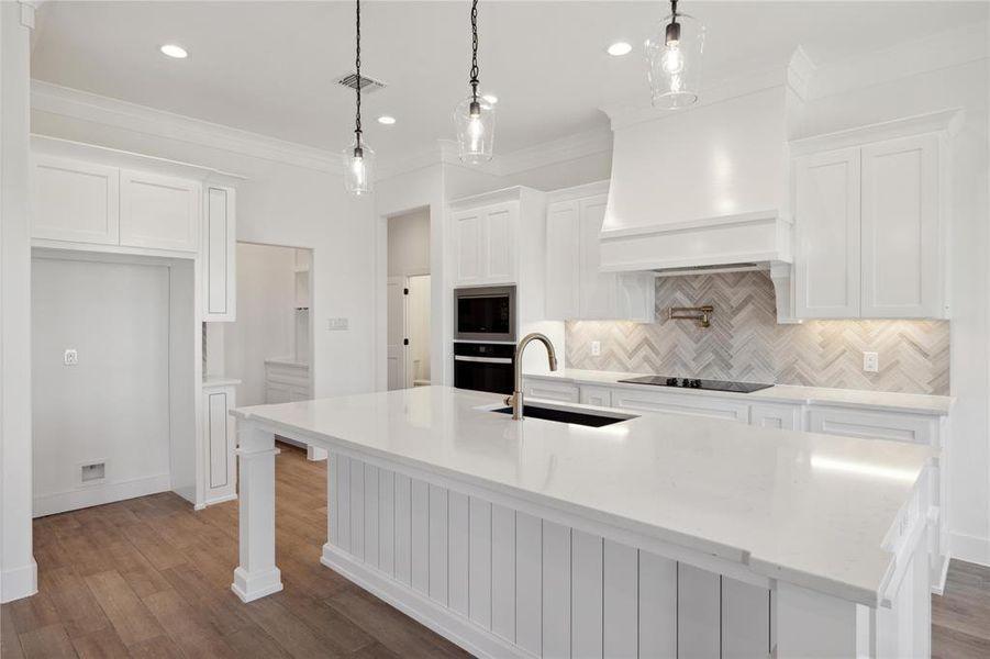 Kitchen featuring white cabinetry, tasteful backsplash, premium range hood, and a center island with sink