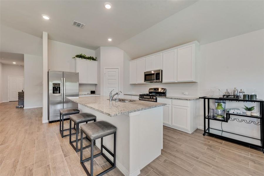 Kitchen with white cabinetry, appliances with stainless steel finishes, recessed lighting, light stone counters, and a kitchen bar Kitchen with white cabinetry, appliances with stainless steel finishes, recessed lighting, light stone counters, and a kitchen bar