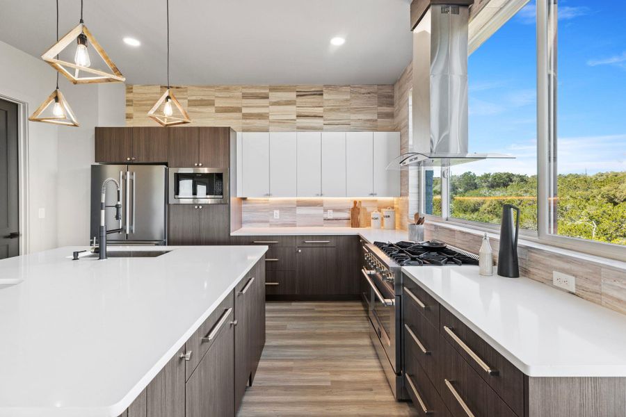 Kitchen featuring a sink, wall chimney range hood, backsplash, appliances with stainless steel finishes, and light countertops