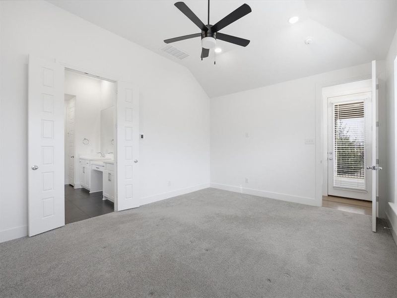 Unfurnished Primary bedroom featuring dark carpet, vaulted ceiling, ceiling fan, and ensuite bathroom