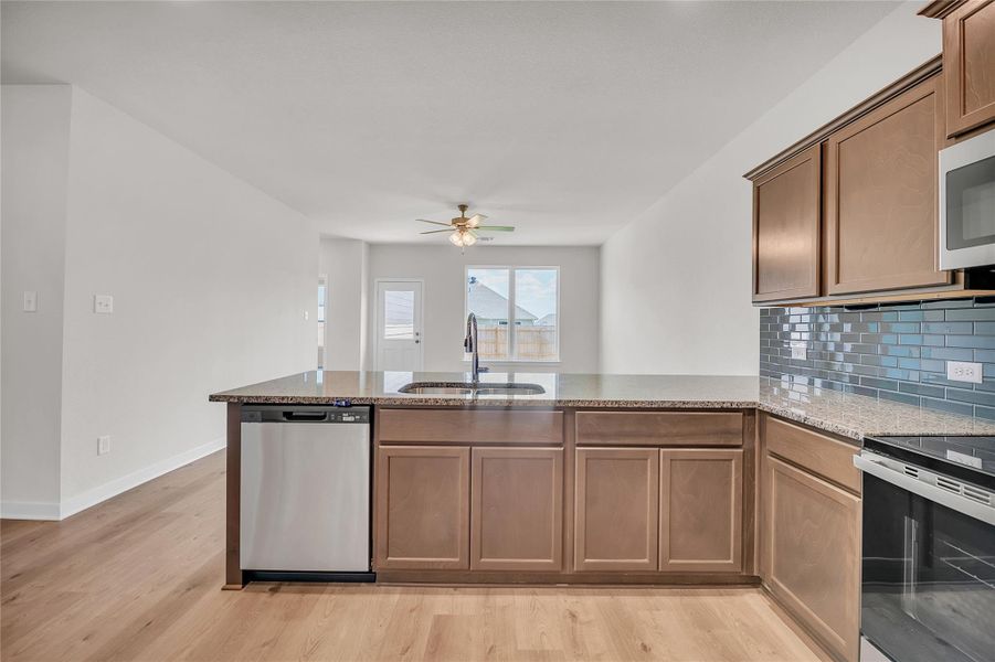 Kitchen featuring appliances with stainless steel finishes, light stone countertops, light wood-type flooring, backsplash, and a peninsula Kitchen featuring appliances with stainless steel finishes, light stone countertops, light wood-type flooring, backsplash, and a peninsula