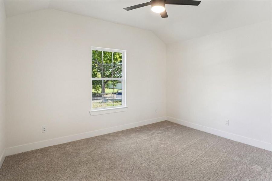 Spare room featuring vaulted ceiling, carpet, and a ceiling fan Spare room featuring vaulted ceiling, carpet, and a ceiling fan