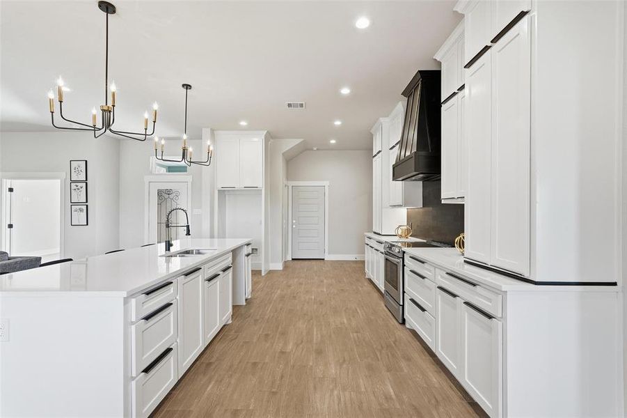 Kitchen with an island with sink, stainless steel electric range oven, white cabinetry, light wood-style floors, and recessed lighting
