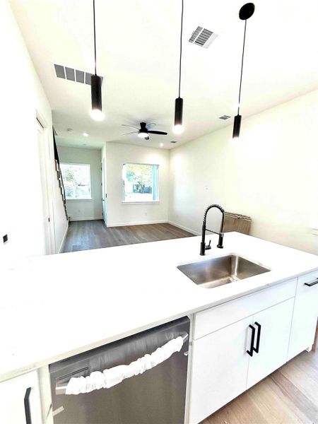 Kitchen featuring white cabinetry, light wood-type flooring, hanging light fixtures, dishwasher, and open floor plan