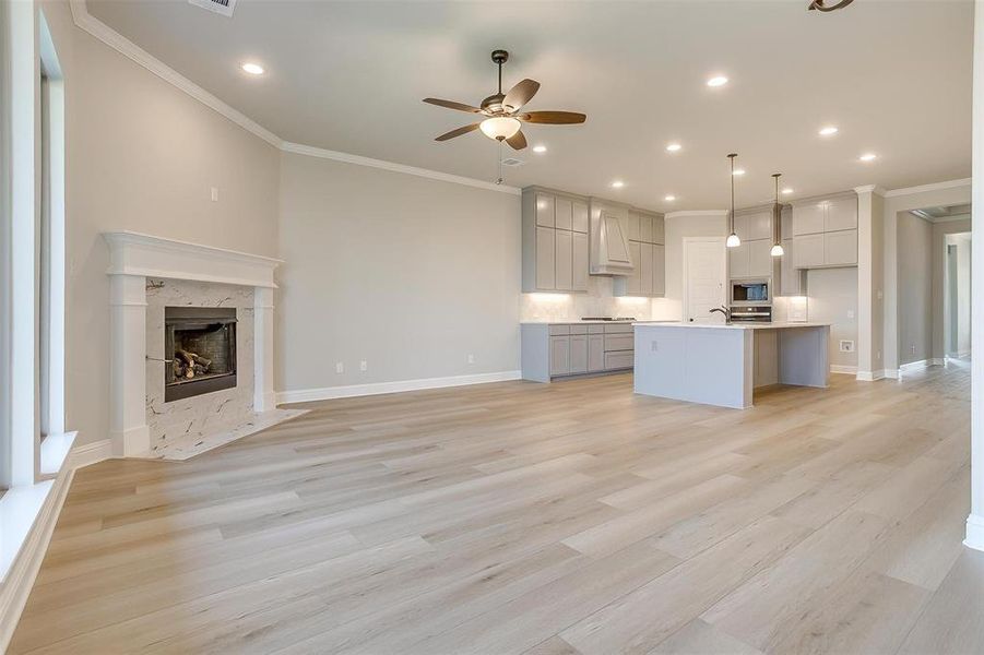 Kitchen with light wood-type flooring, a kitchen island with sink, hanging light fixtures, and ceiling fan