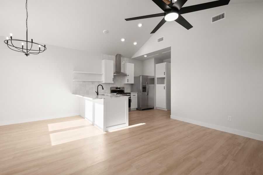 Kitchen featuring white cabinets, stainless steel appliances, suspended lighting, a peninsula, and vaulted ceiling