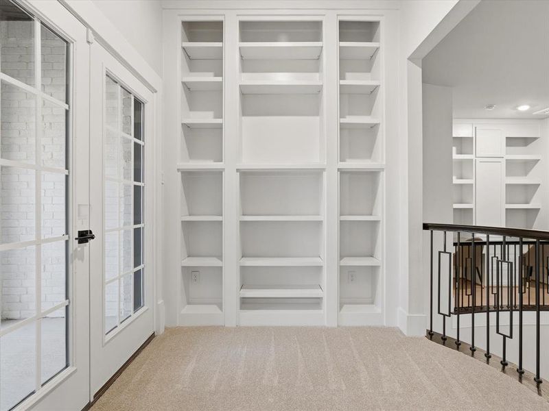 Built-in shelving with multiple compartments, French doors with grid-patterned glass, light-colored carpeting, and a wrought iron railing with geometric designs Built-in shelving with multiple compartments, French doors with grid-patterned glass, light-colored carpeting, and a wrought iron railing with geometric designs
