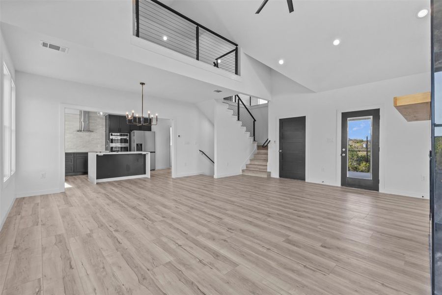 Unfurnished living room with hanging lights, light wood-style floors, vaulted ceiling, and ceiling fan