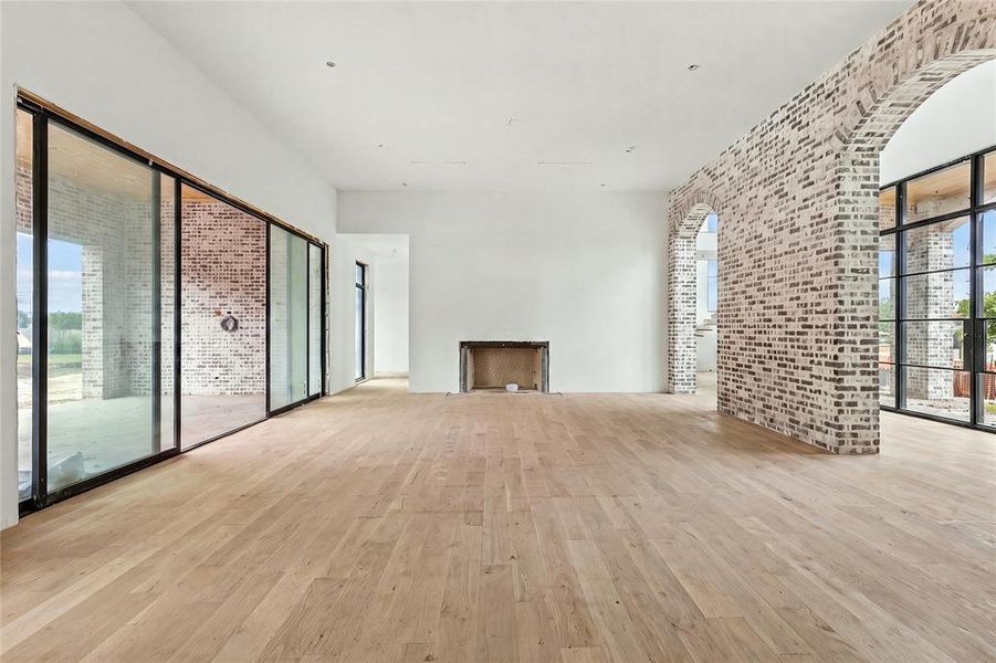Spacious room featuring light wood-finish flooring, white walls, and a prominent brick accent wall with arched openings