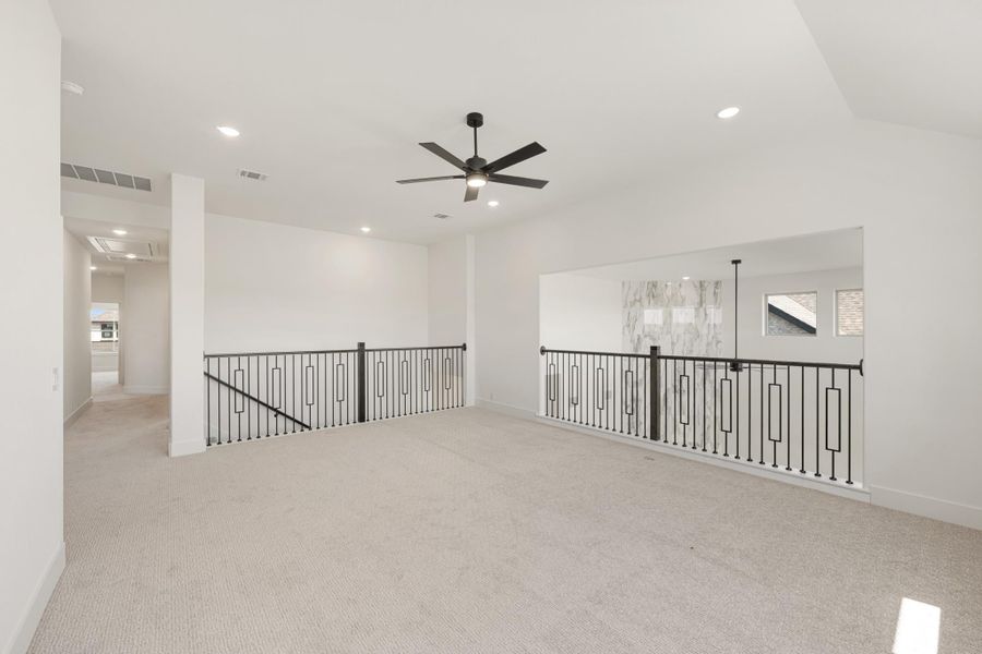 Open upstairs loft with carpet, black ceiling fan, and wrought iron stair railings overlooking lower level