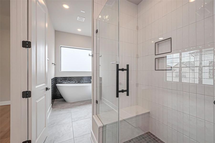 Experience luxury in this modern bathroom, featuring a spacious glass shower, sleek white tiles, and elegant built-in shelving. A freestanding tub by a frosted window bathes the space in natural light, creating a serene, spa-like retreat.