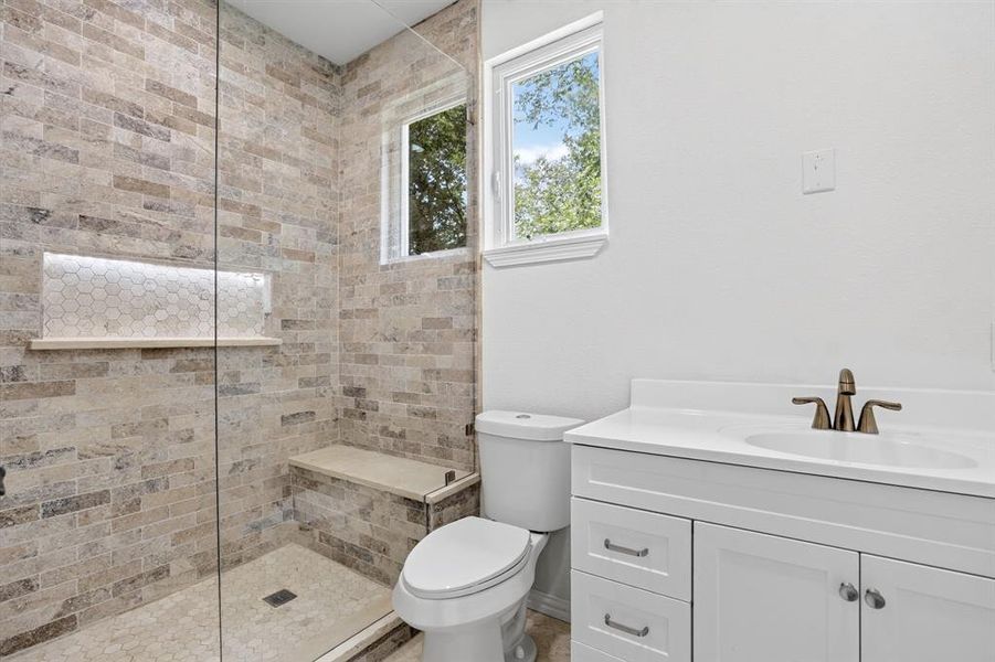Bathroom featuring a walk-in shower with natural stone tile, a built-in shower bench, and an illuminated shower niche