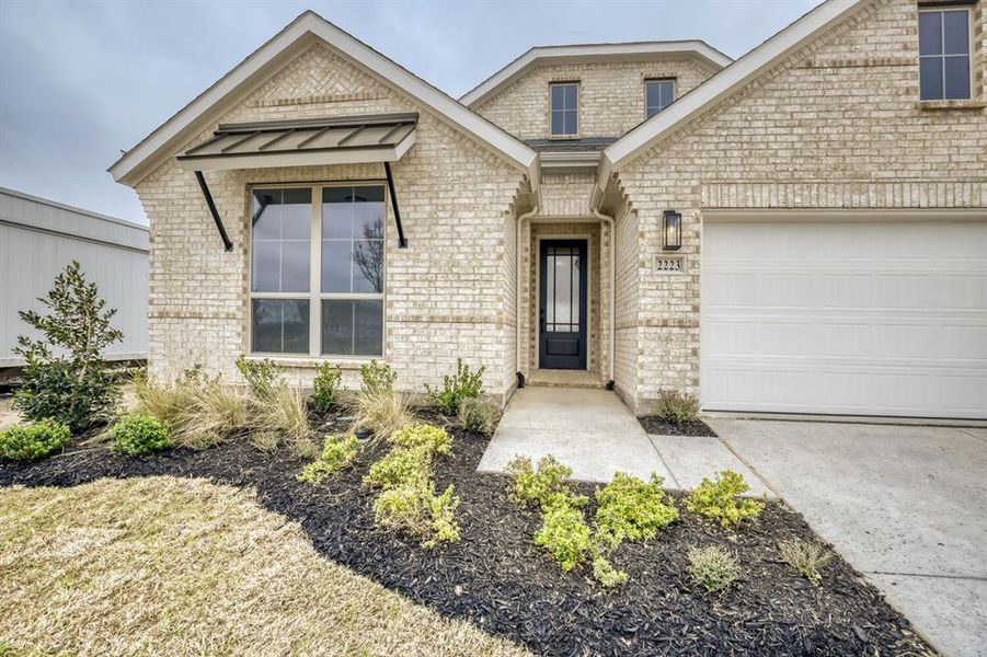 View of exterior entry with brick siding, a standing seam roof, an attached garage, and concrete driveway