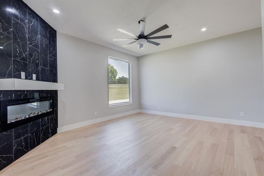 Feature wall with dark tile surround and integrated linear fireplace, light wood-finish flooring, recessed lighting, ceiling fan, and a large window