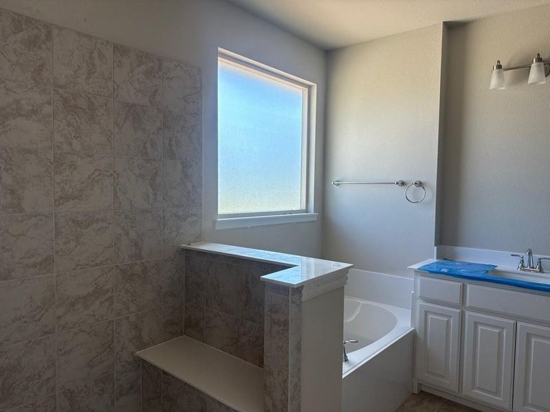 Bathroom featuring a built-in tub, white vanity with a single sink, tile flooring, and a frosted window Bathroom featuring a built-in tub, white vanity with a single sink, tile flooring, and a frosted window