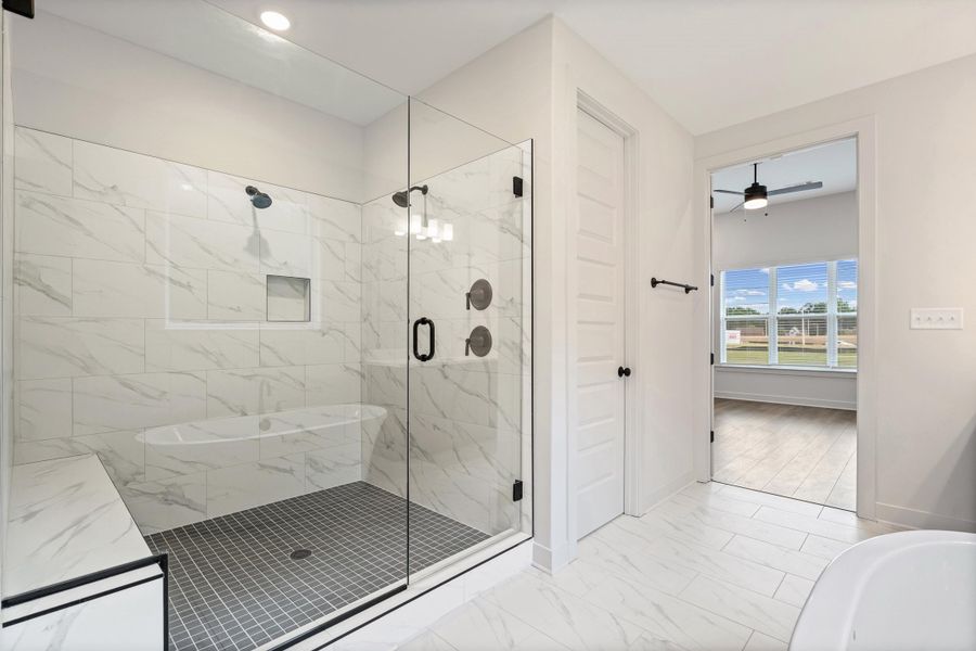 Spacious bathroom featuring a glass-enclosed shower with black fixtures, a built-in shower bench, and a tiled niche Spacious bathroom featuring a glass-enclosed shower with black fixtures, a built-in shower bench, and a tiled niche