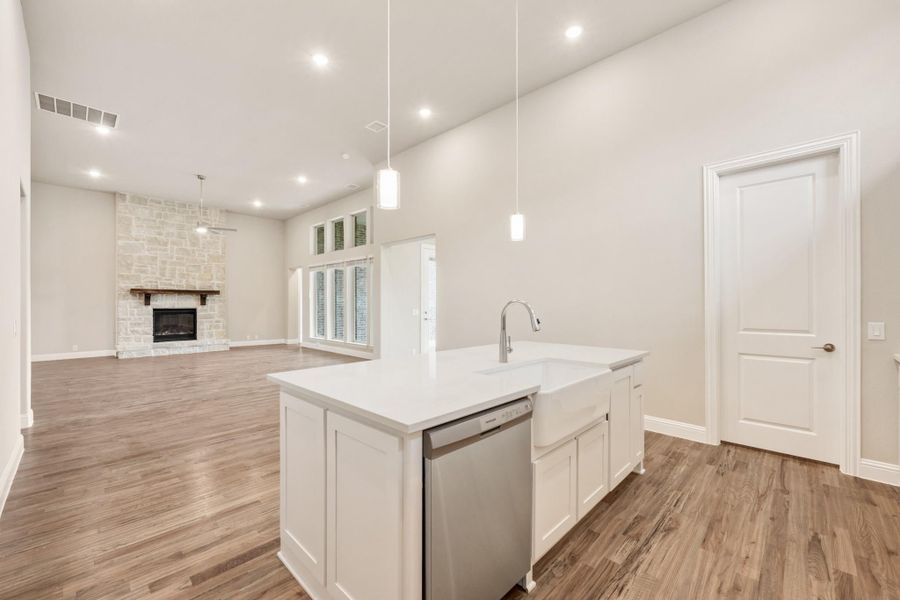 Kitchen island with farmhouse sink and dishwasher, open to living room with stone fireplace and hardwood floors