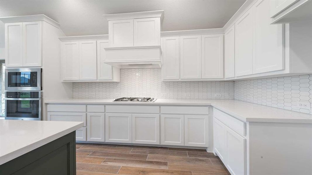 Kitchen with decorative backsplash, appliances with stainless steel finishes, custom range hood, wood-type flooring, and white cabinetry