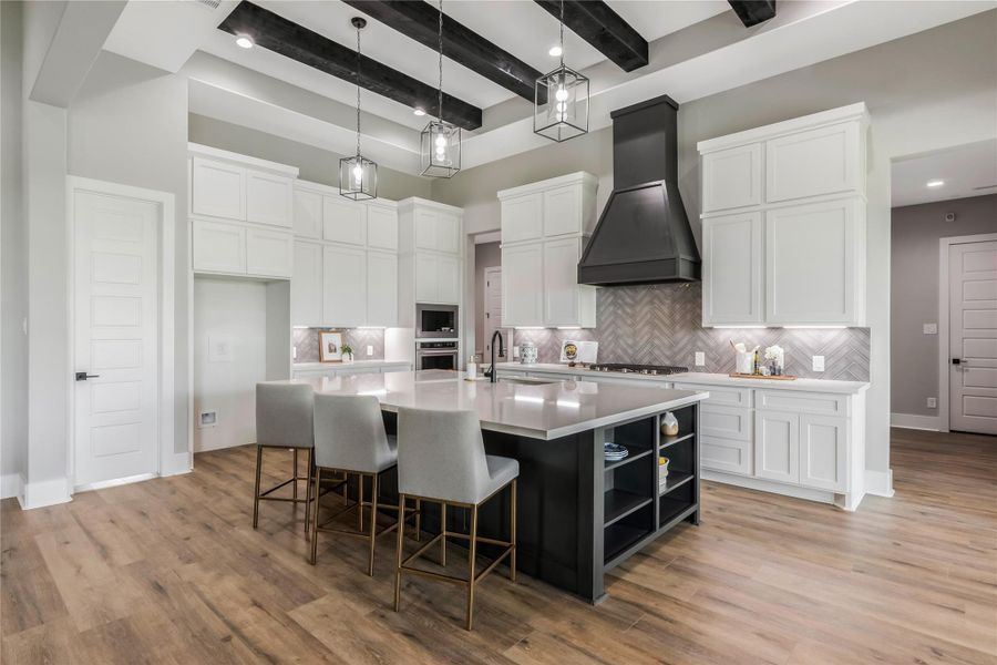 This modern kitchen features a spacious island with seating, elegant pendant lighting, and sleek white cabinetry, while dark ceiling beams add contrast This modern kitchen features a spacious island with seating, elegant pendant lighting, and sleek white cabinetry, while dark ceiling beams add contrast